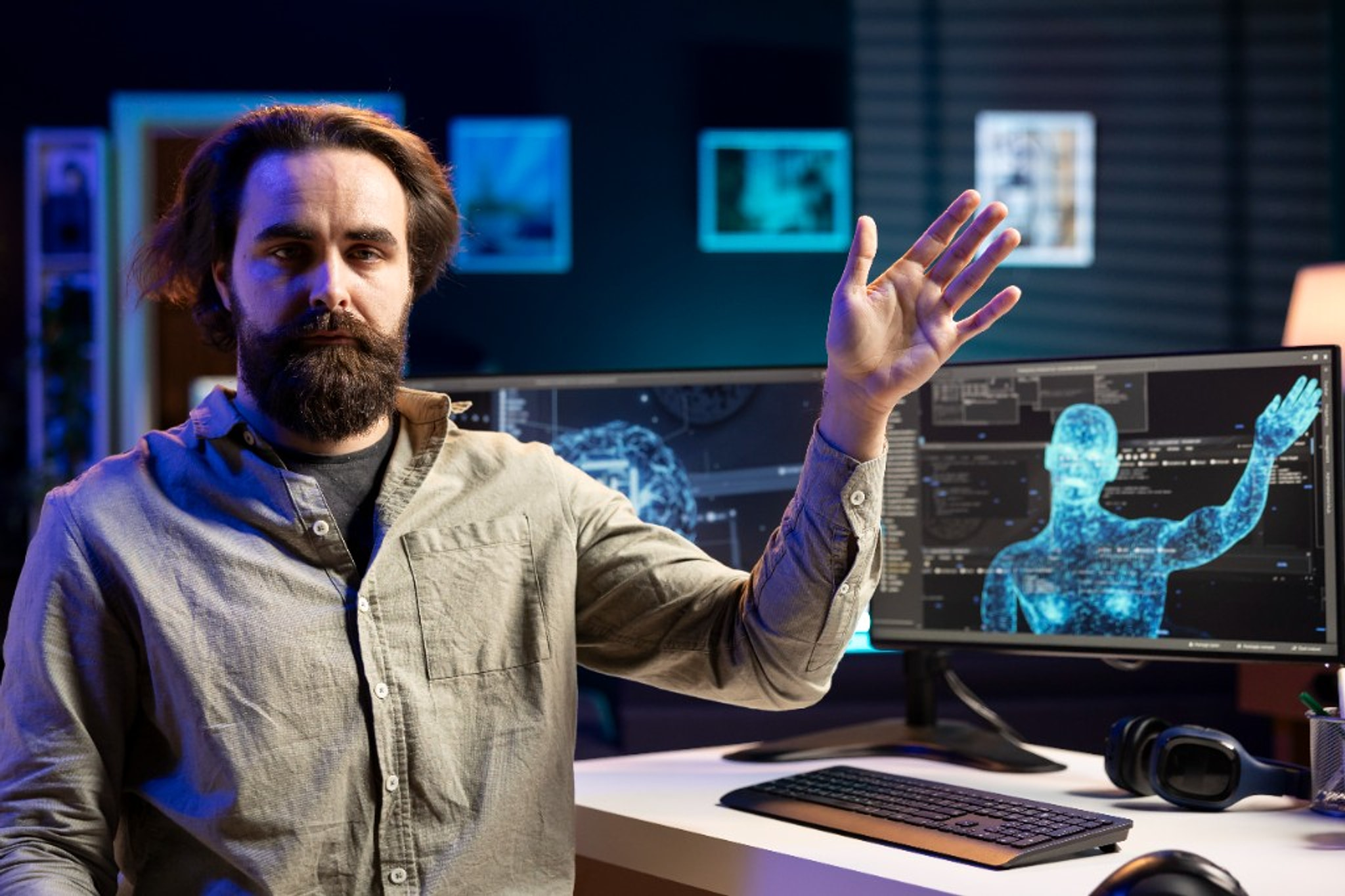 A man at a desk raises his hand toward a glowing blue figure on the monitor.